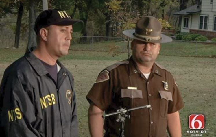 TV screen shot with Aaron Sauer and local law enforcement with woods in the background