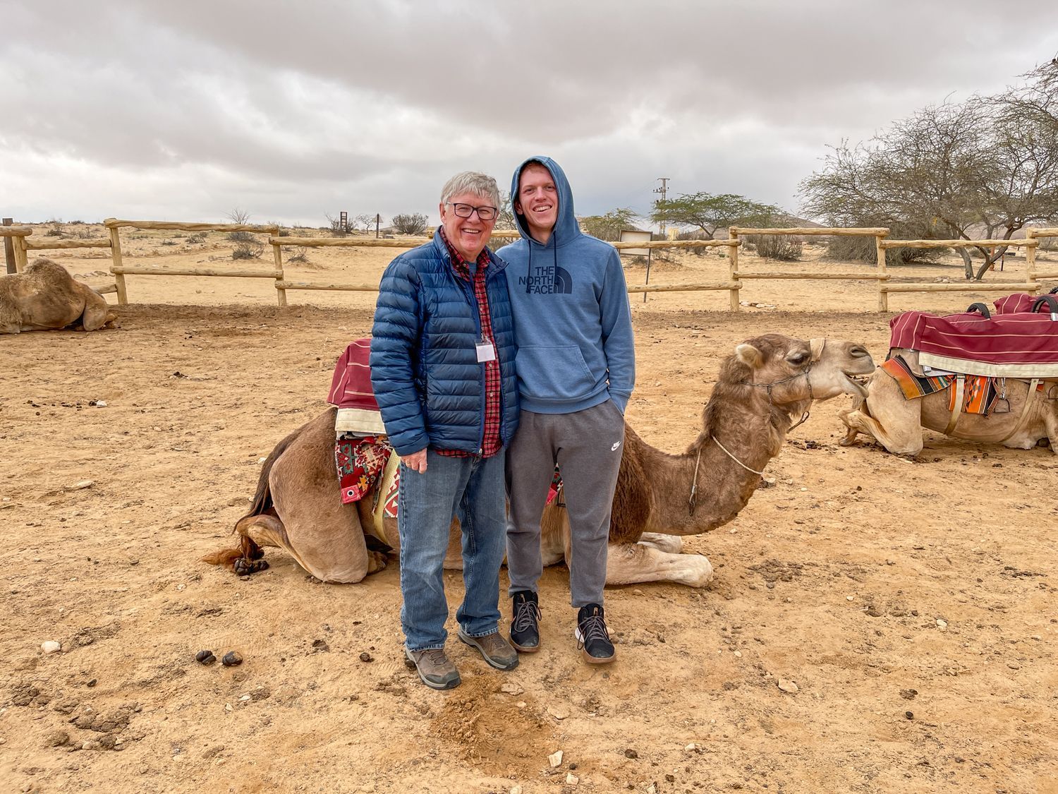 Dan Flynn and Ryan Blobe with their arms around each other, in front of a camel in the Negev Desert