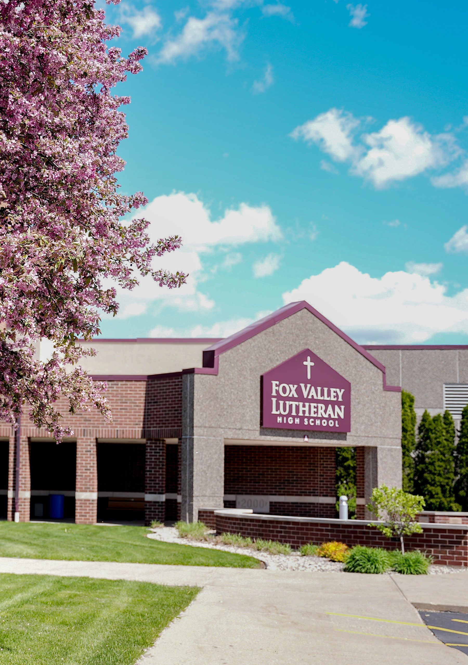 Tower entrance of the school. Sky is a beautiful blue. Grass is green. Trees are in the foreground on the left