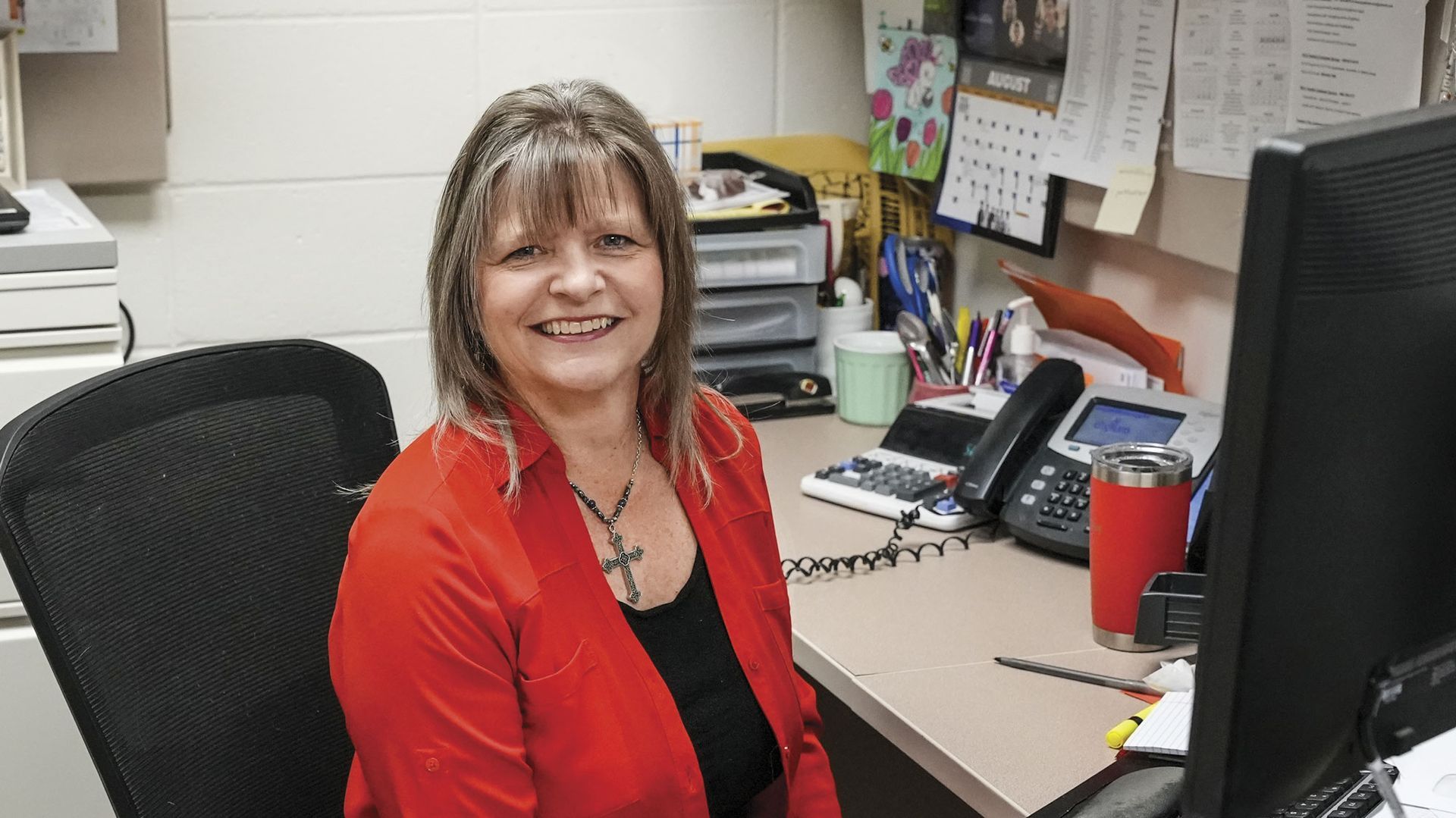Smiling Krista Davis in red shirt, sitting at her desk