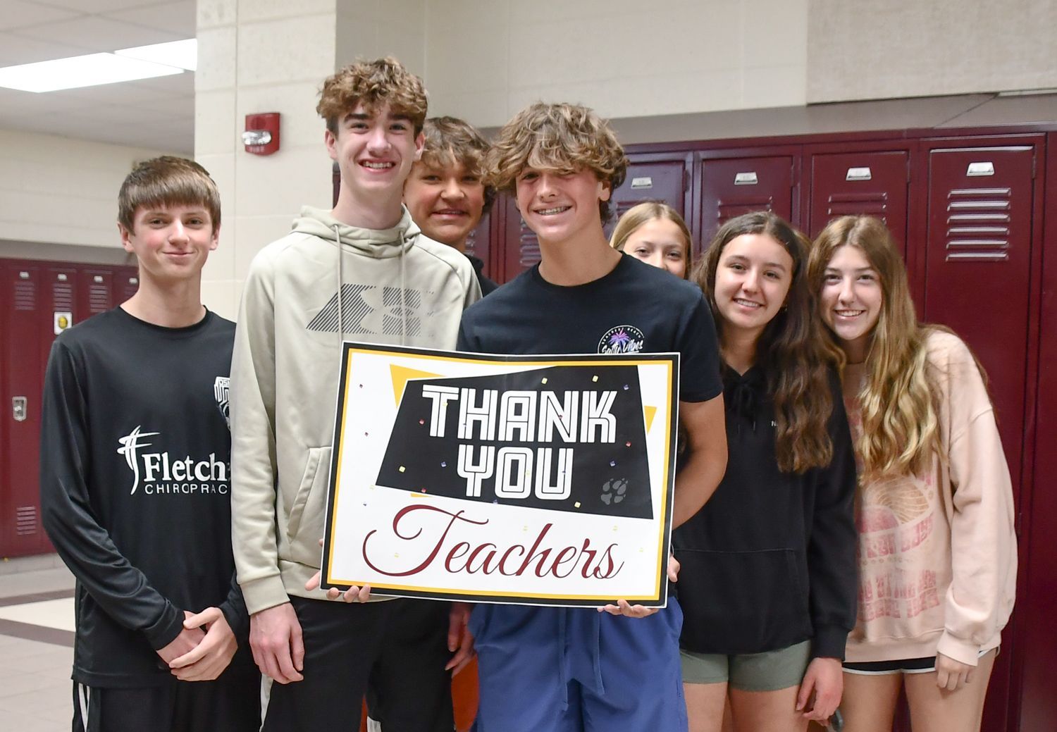 Group of boy and girl students in the locker hallway at FVL, holding a sign that says 