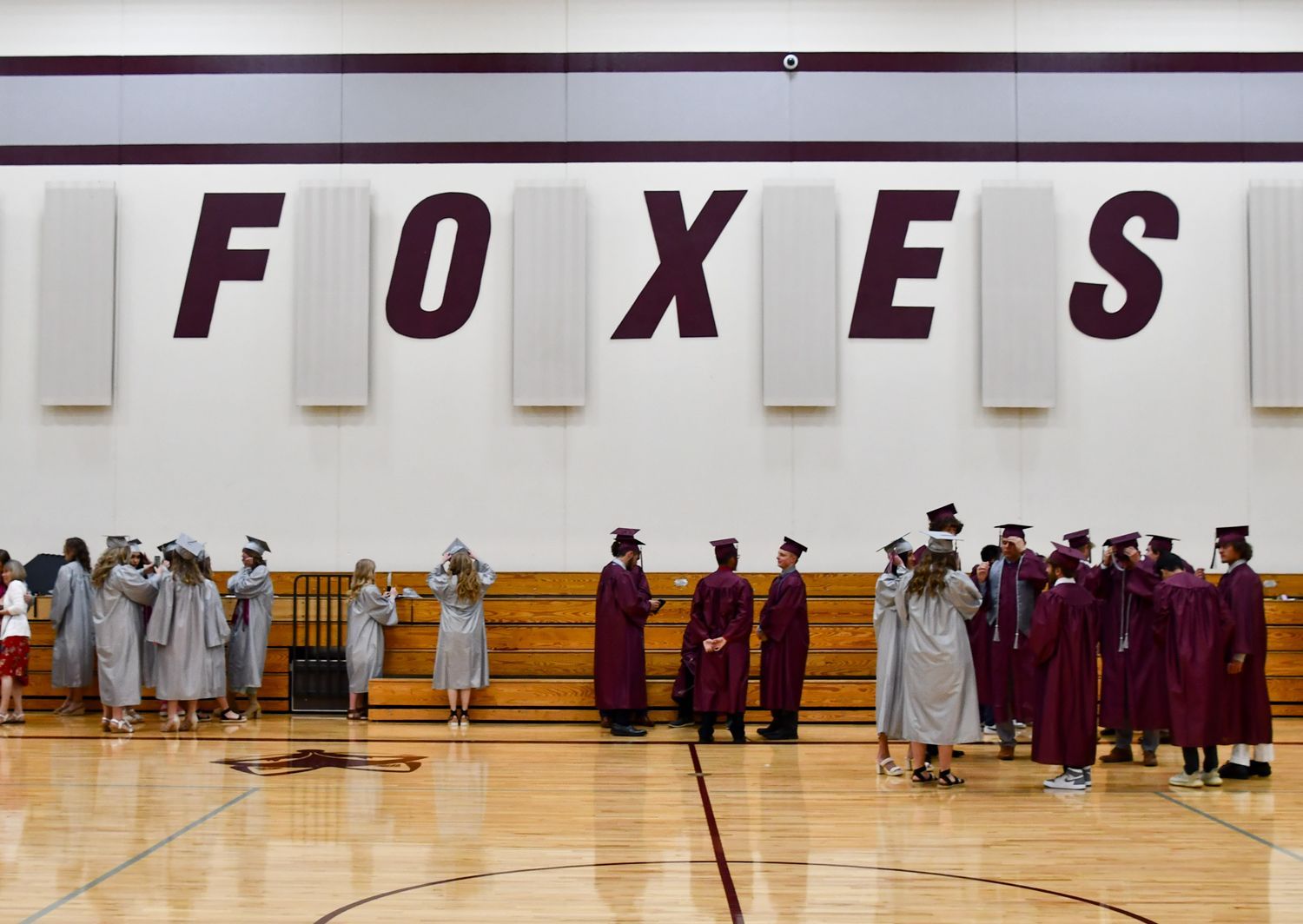 Pre-graduation in the small gym. Guys and girls in cap and gown with the word FOXES on the wall behind them