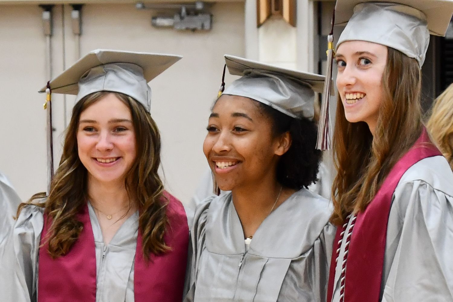 Side view of three smiling girls in cap and gown. 
