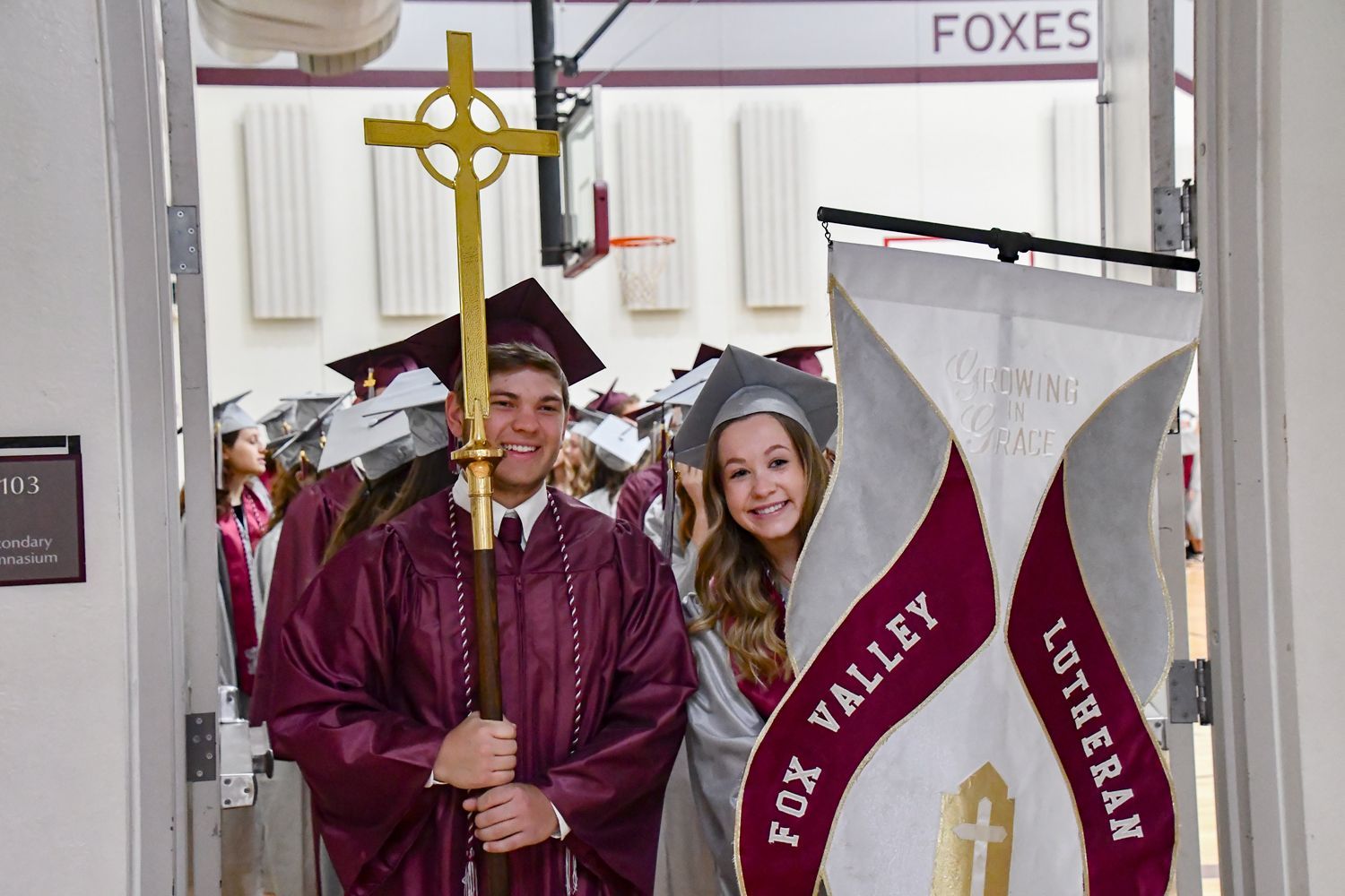 Guy and girl holding the cross and FVL Banner at the head of the line of students for the processional