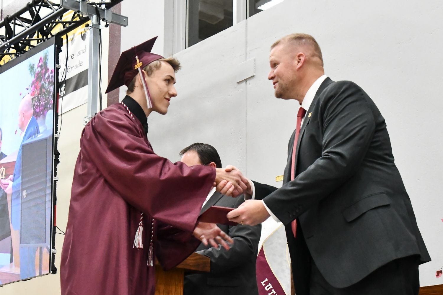 President Loberger shaking the hand of a male student, and handing him a diploma