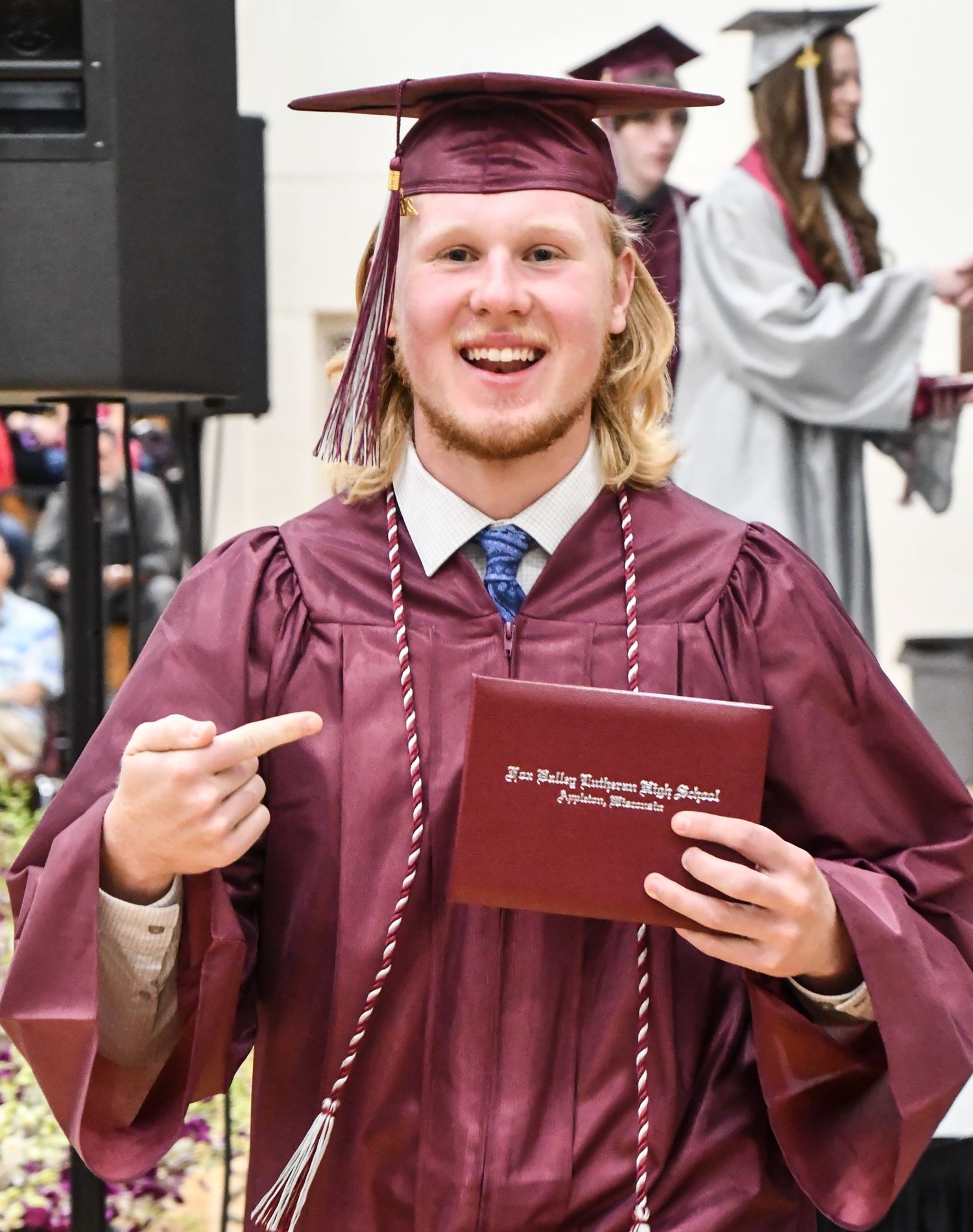 Happy male student, pointing to his diploma after he got off stage
