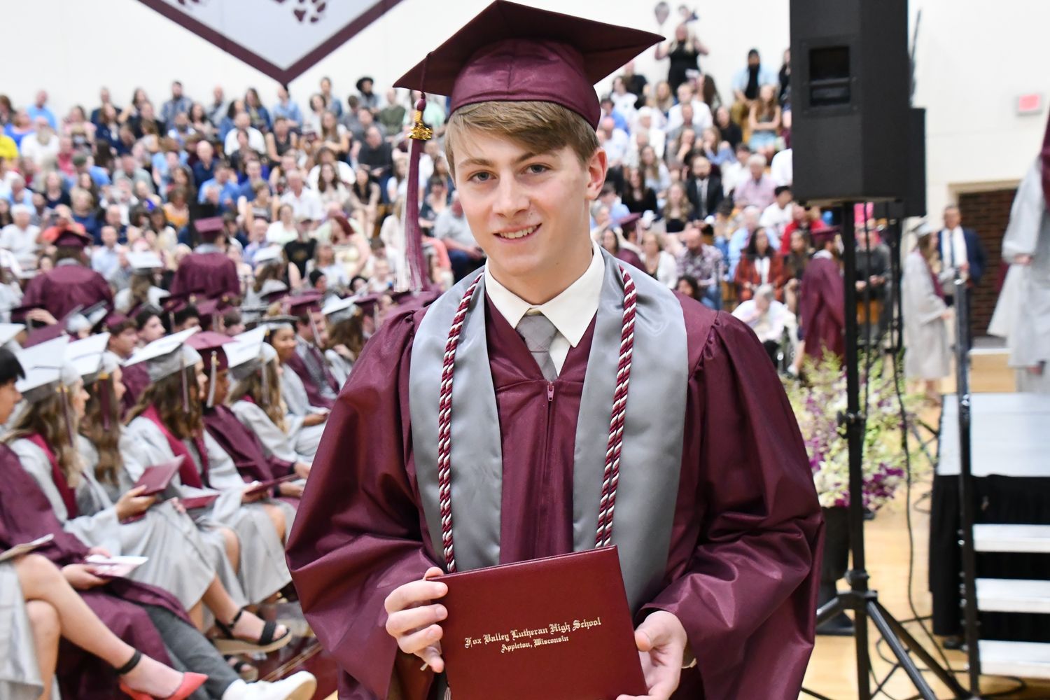 Smiling male student, holding up his diploma after walking off stage