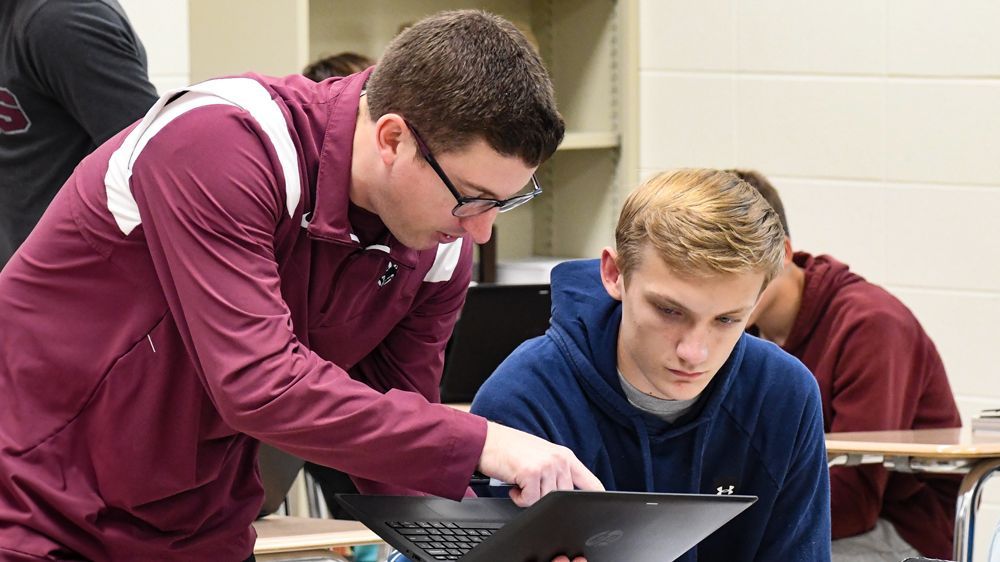 Tommy Stelter helping a student in his class with something on the student's laptop.