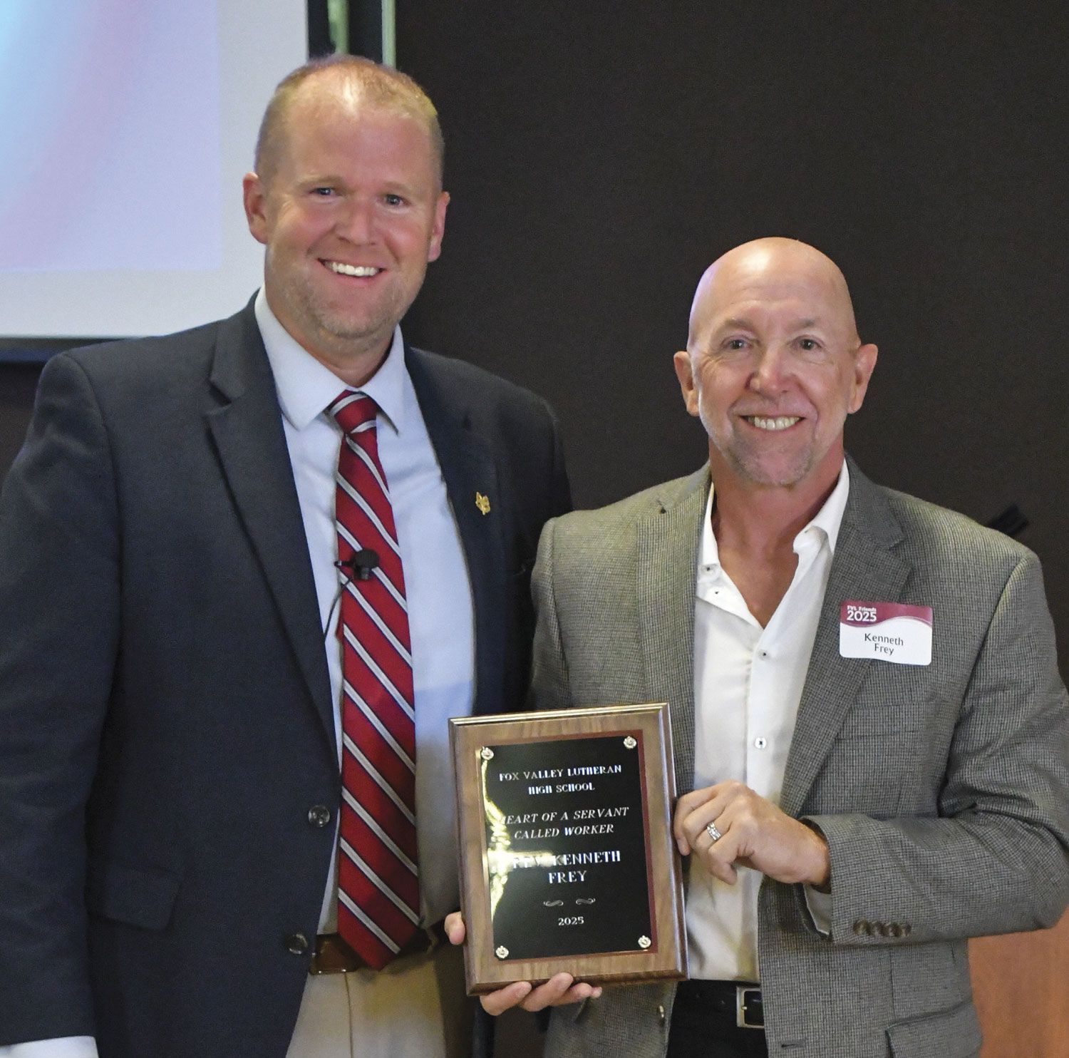 President Loberger smiling and standing by a happy Rev. Ron Ash who is holding up his Heart of a Servant plaque
