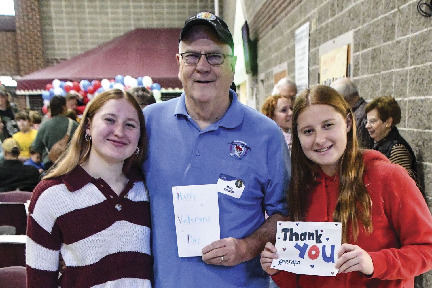 Smiling male veteran with a smiling granddaughter on each side. Two cards displayed that they made for him.