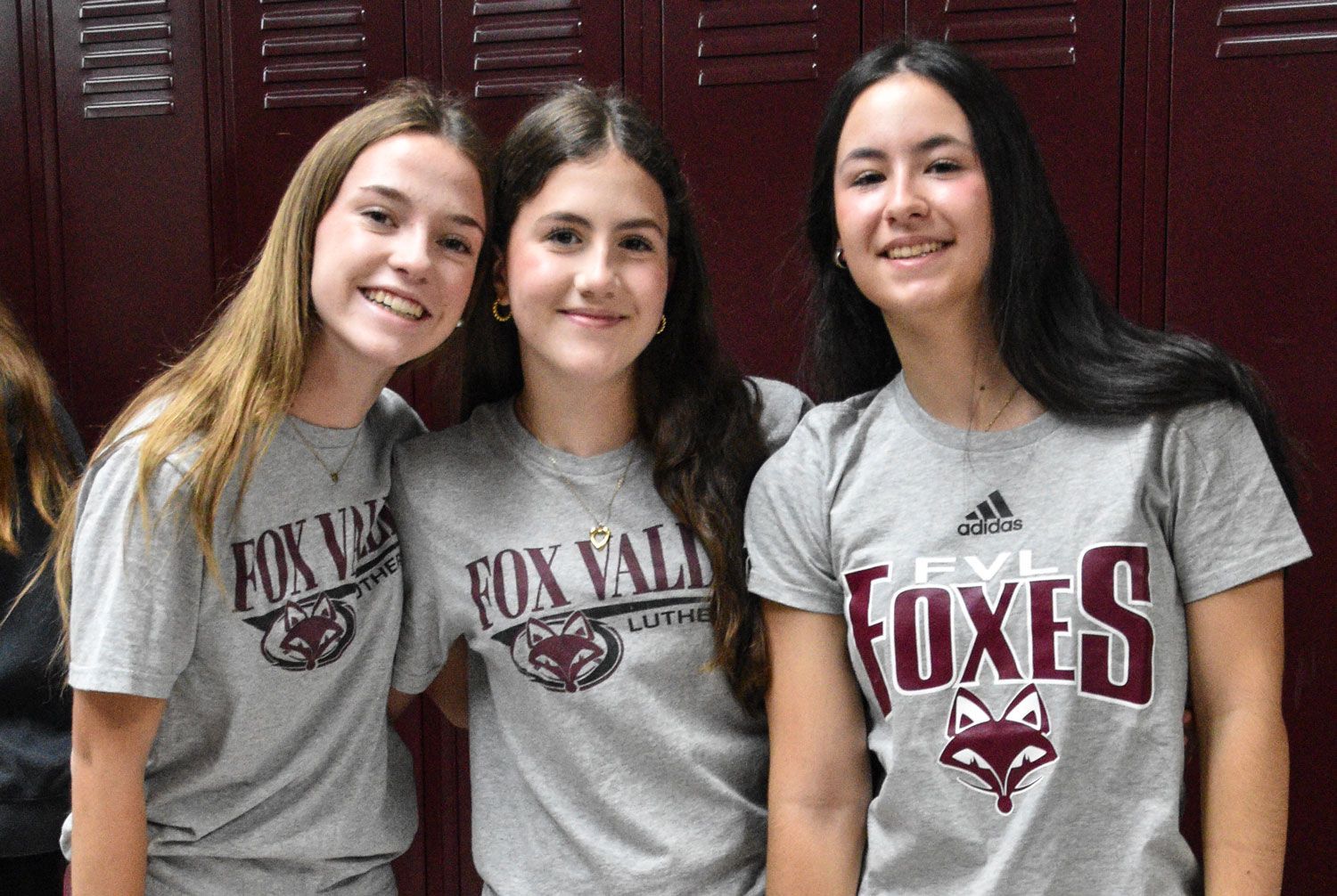 Three smiling girls in FVL Foxes shirts, in front of lockers