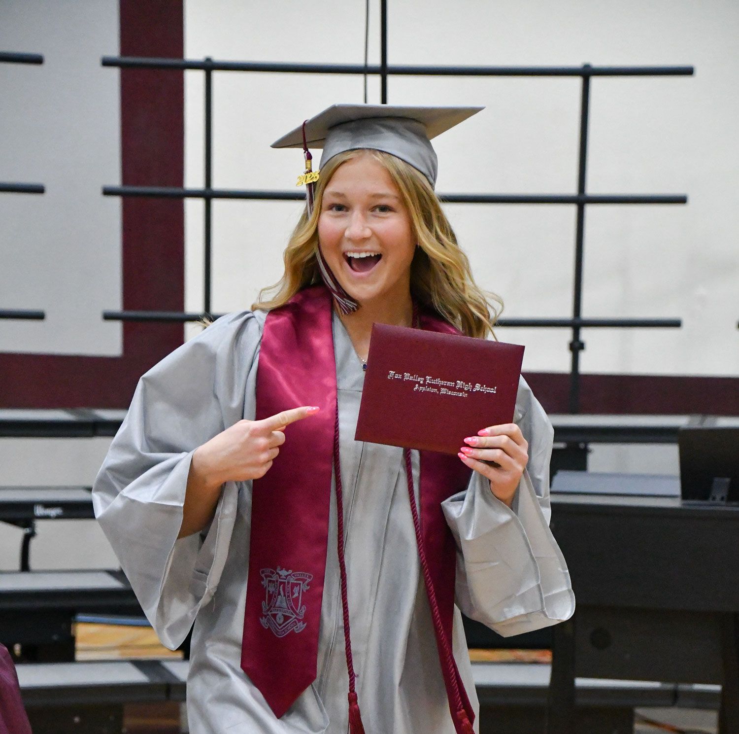 Smiling student, pointing at diploma, as she walks back to her chair