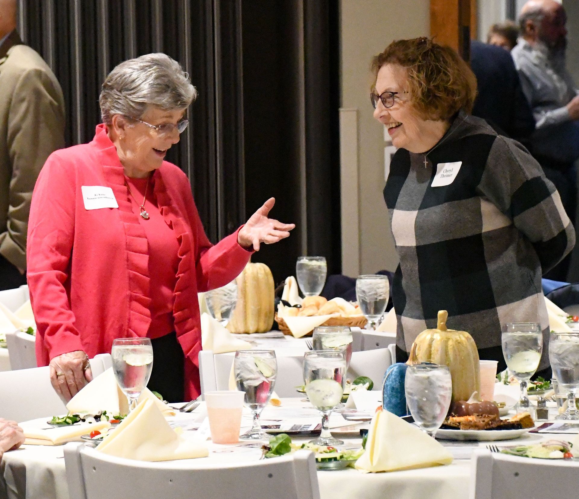Two happy women standing by a table, in conversation
