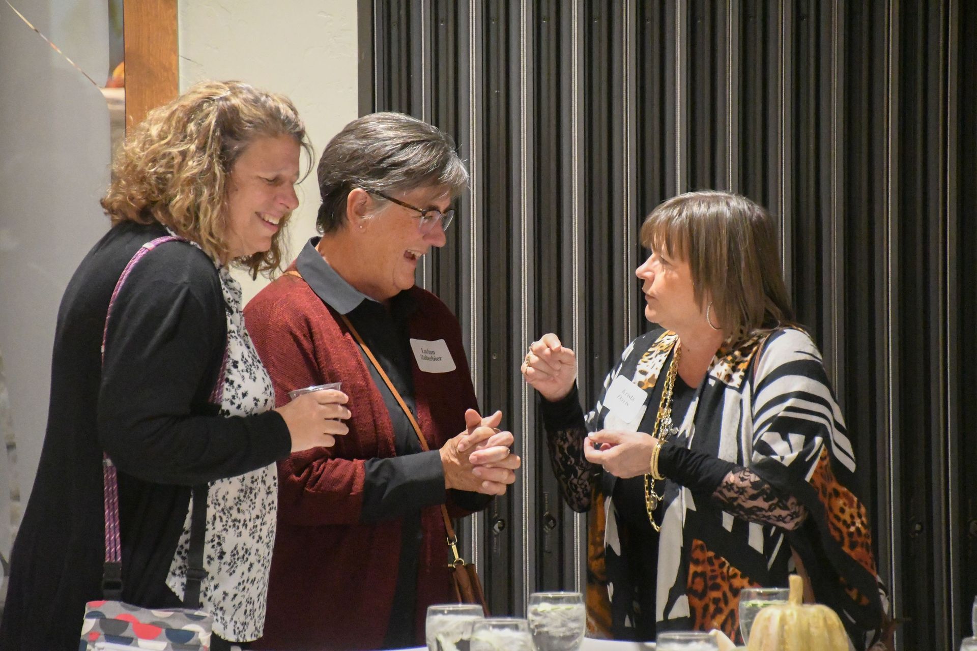 Three women in lively conversation while standing by a table