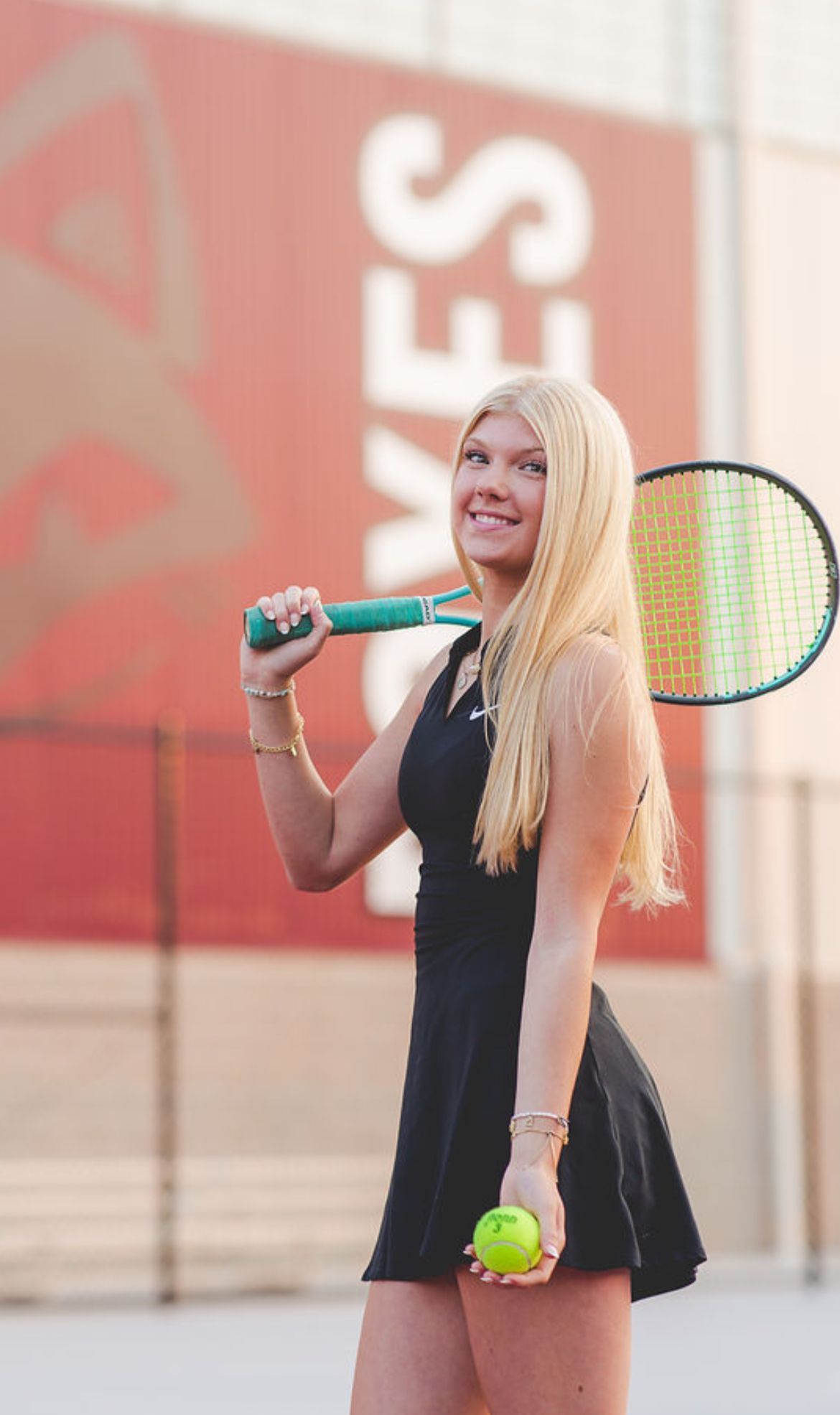 Avery Steffes with tennis racket, by Trout Center, smiling at the camera