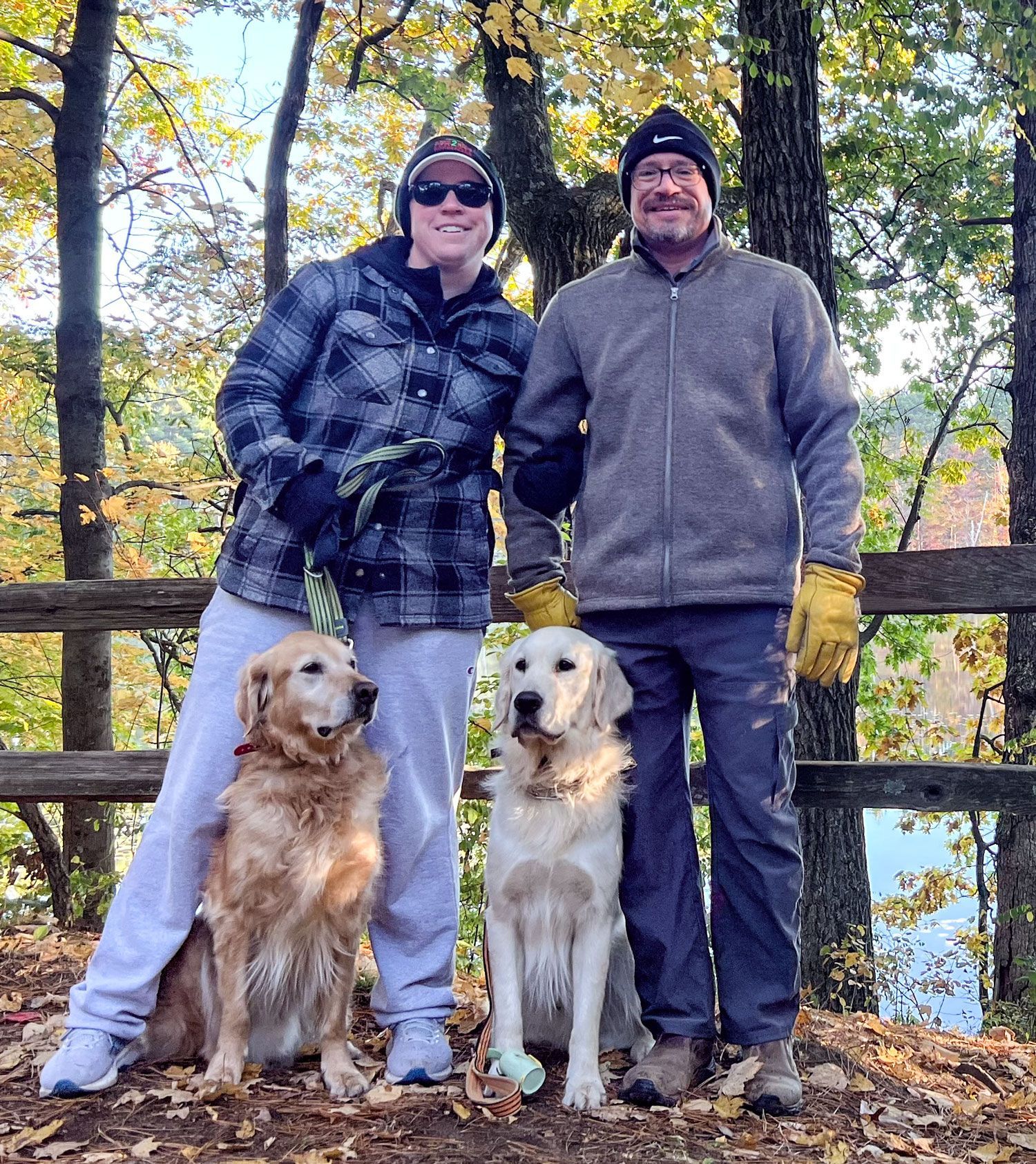 Smiling photo of Rachel, her husband, and their two dogs in the woods in autumn