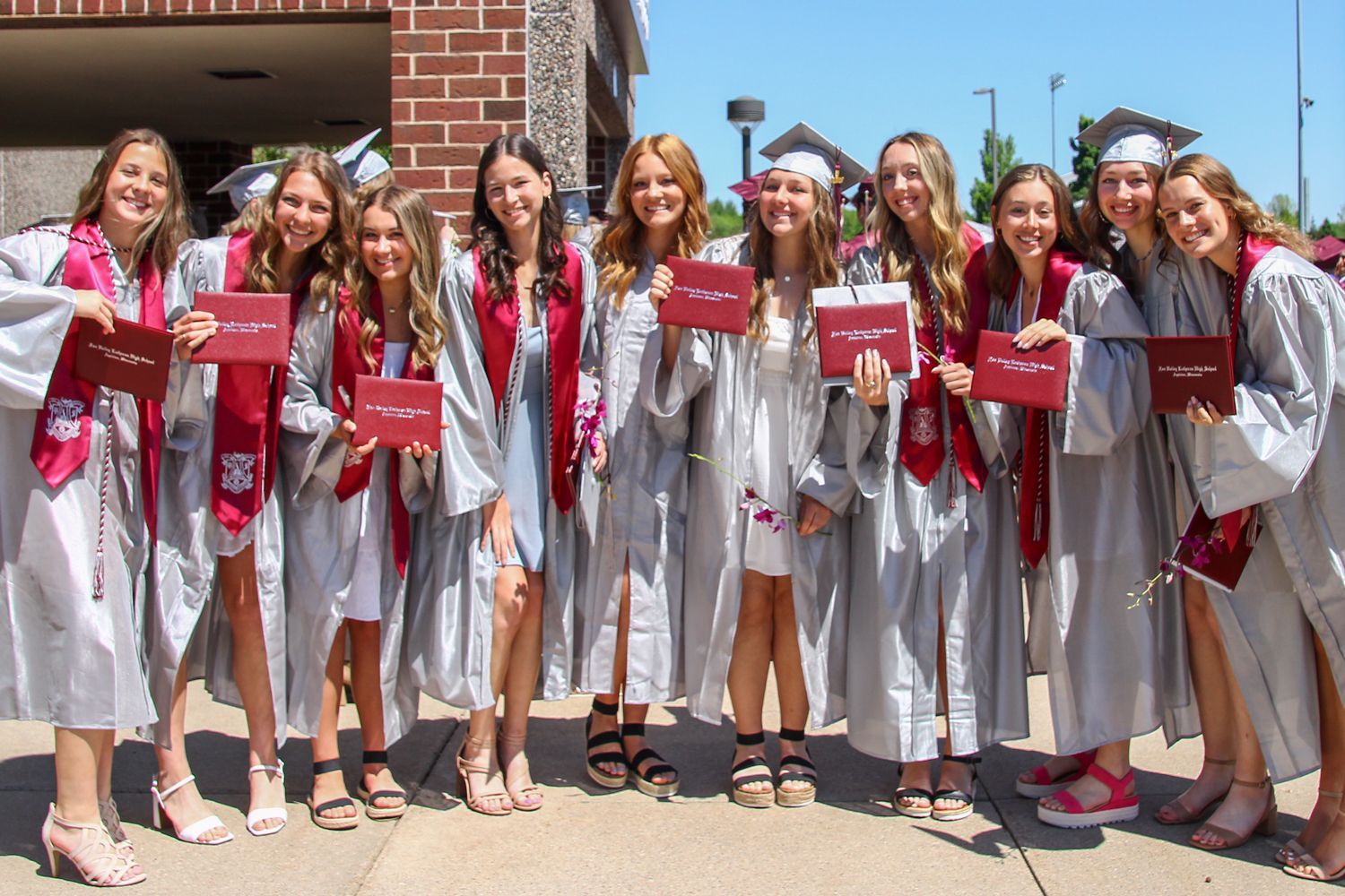 Row of ten girls holding up their diplomas outside, after the ceremony