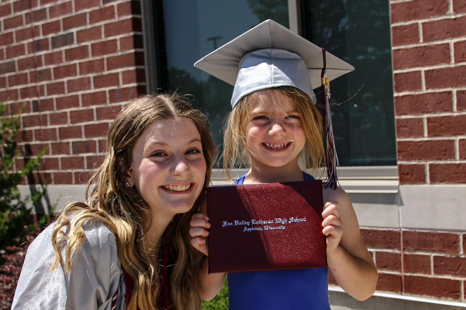 Little girl wearing the cap and holding the diploma of the female graduate who is smiling and is next to her
