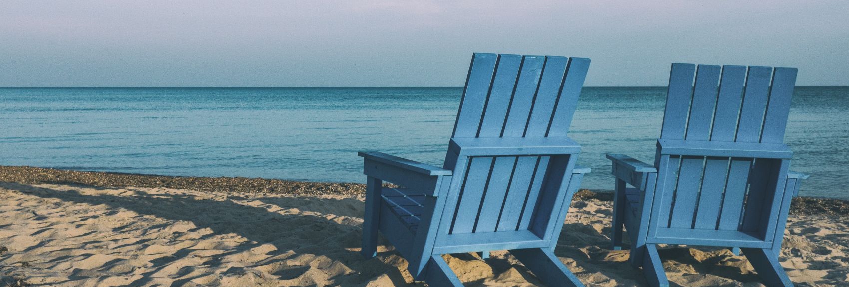 Two blue, empty beach chairs on the sand with the ocean beyond