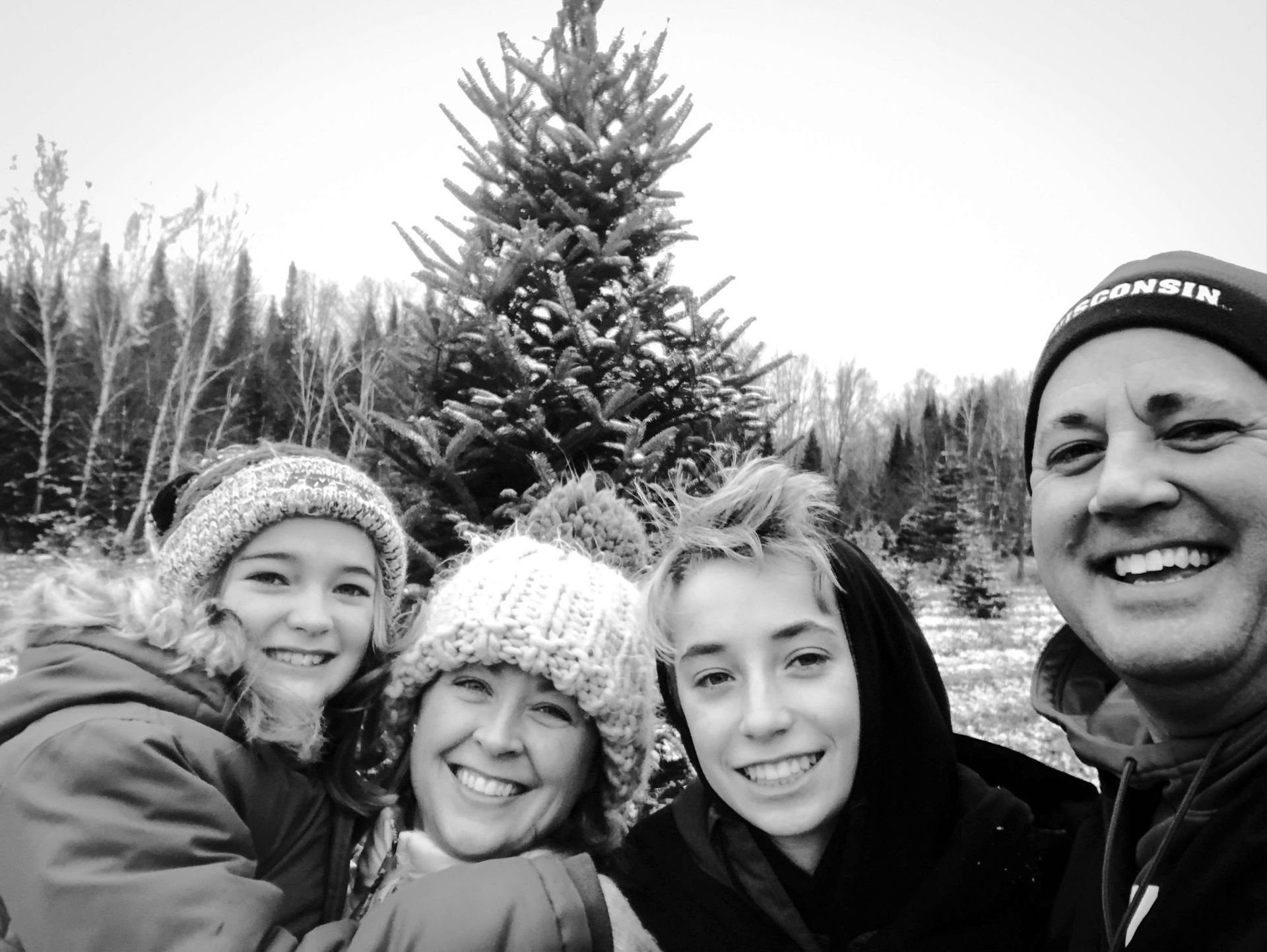 Black and white photo of Aaron with his wife and two children at a Christmas tree farm