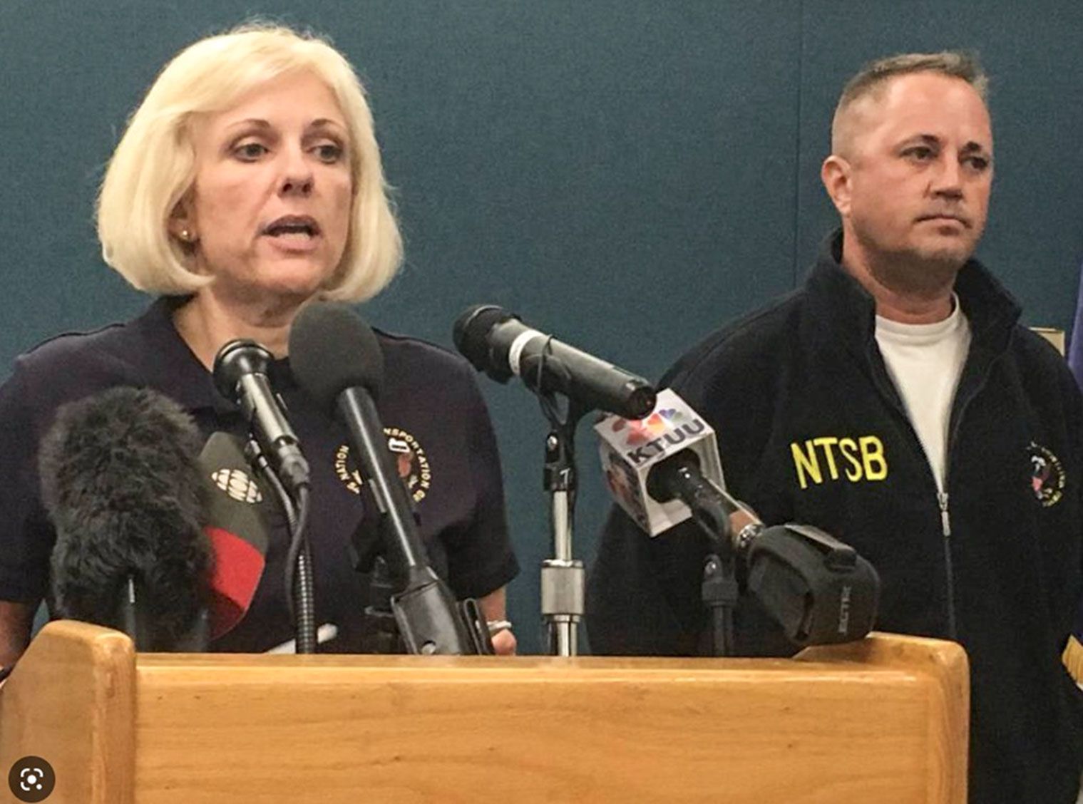 Jennifer Homendy, head of NTSB, speaking at a podium with many microphones, and with Aaron  on her left