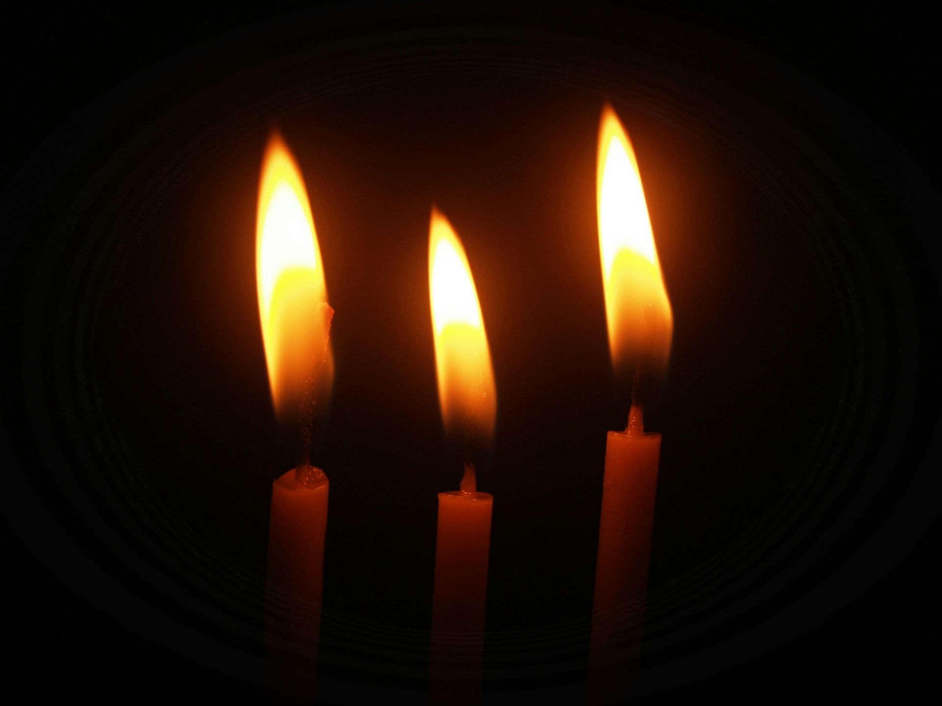Three lit taper candles, surrounded by darkness