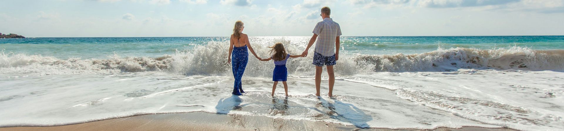 Mom, dad, and child on beach, walking in the surf