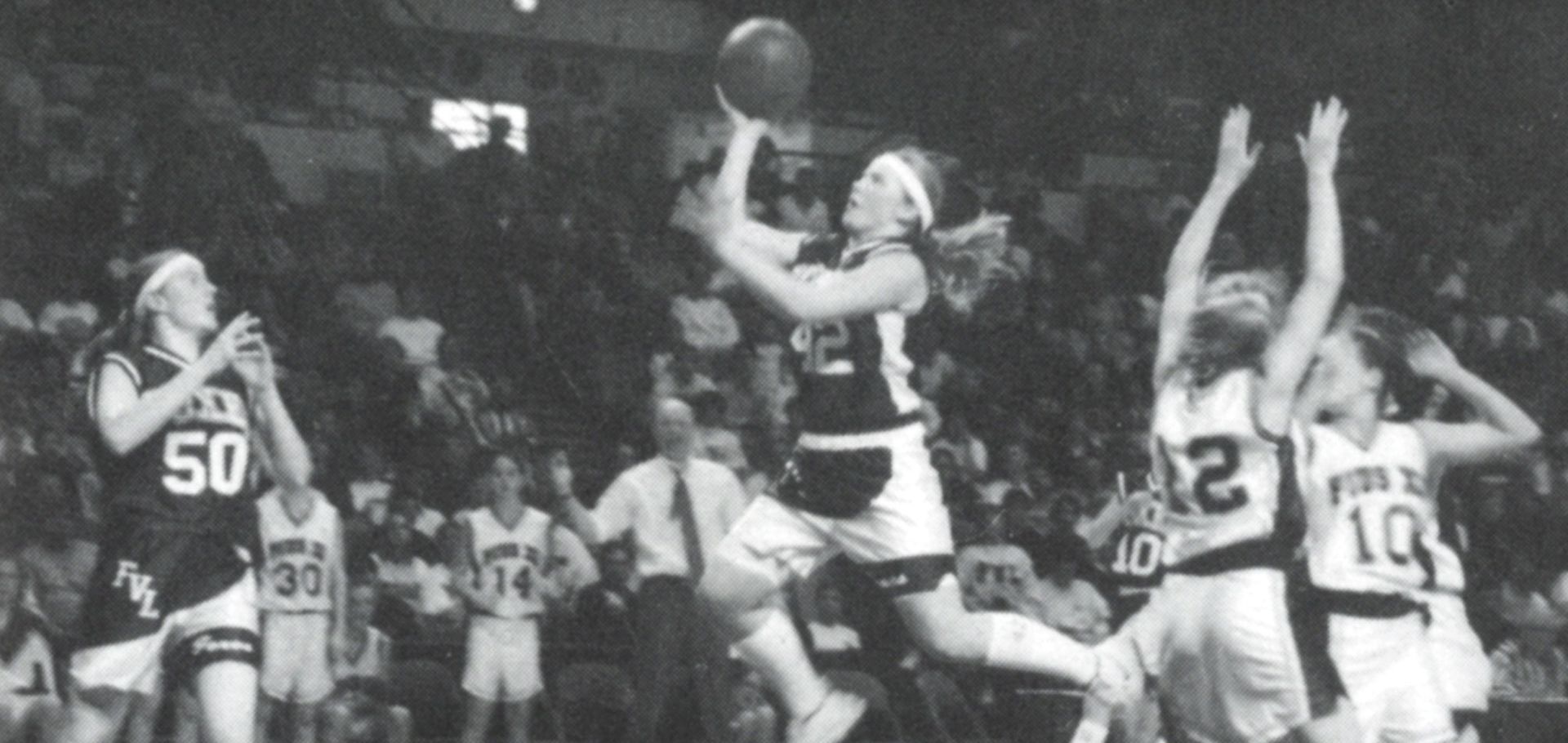 Female team member in the air with the ball up--ready to release to shoot for a basket