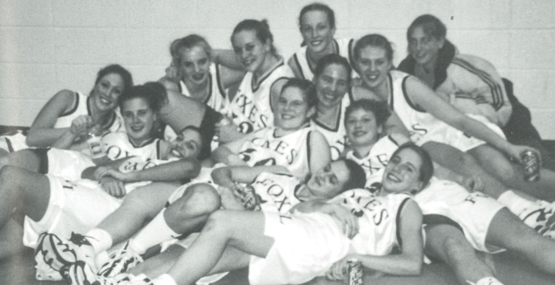 Female basketball team piled on top of each other, smiling at the camera