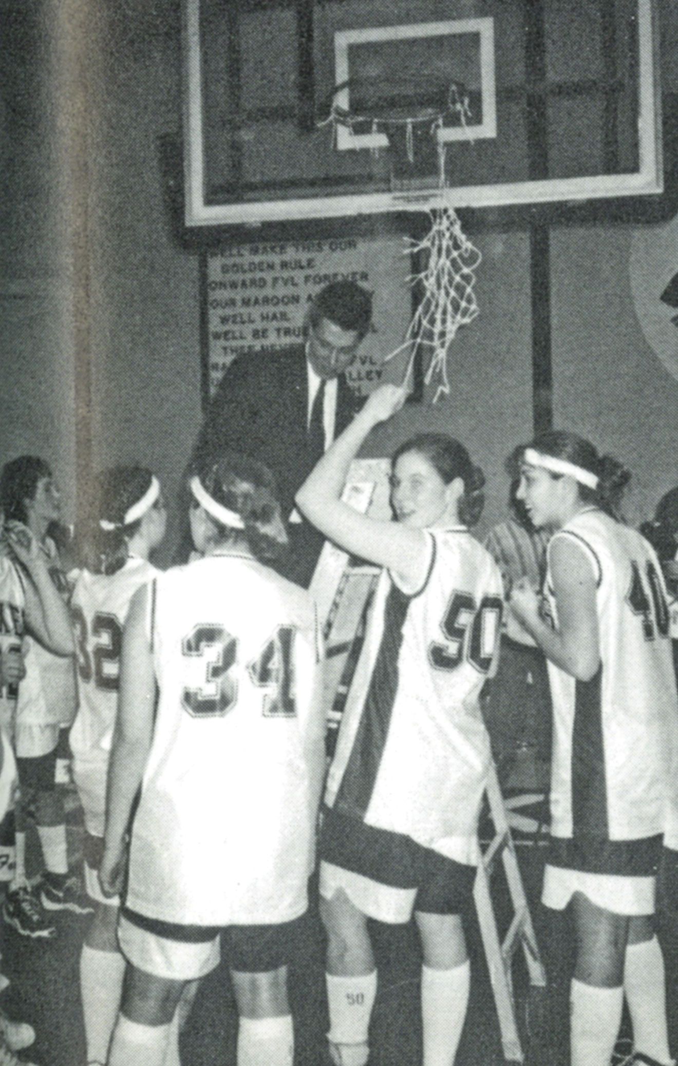 Coach Wenzel and female basketball team cutting down the net after a significant victory.