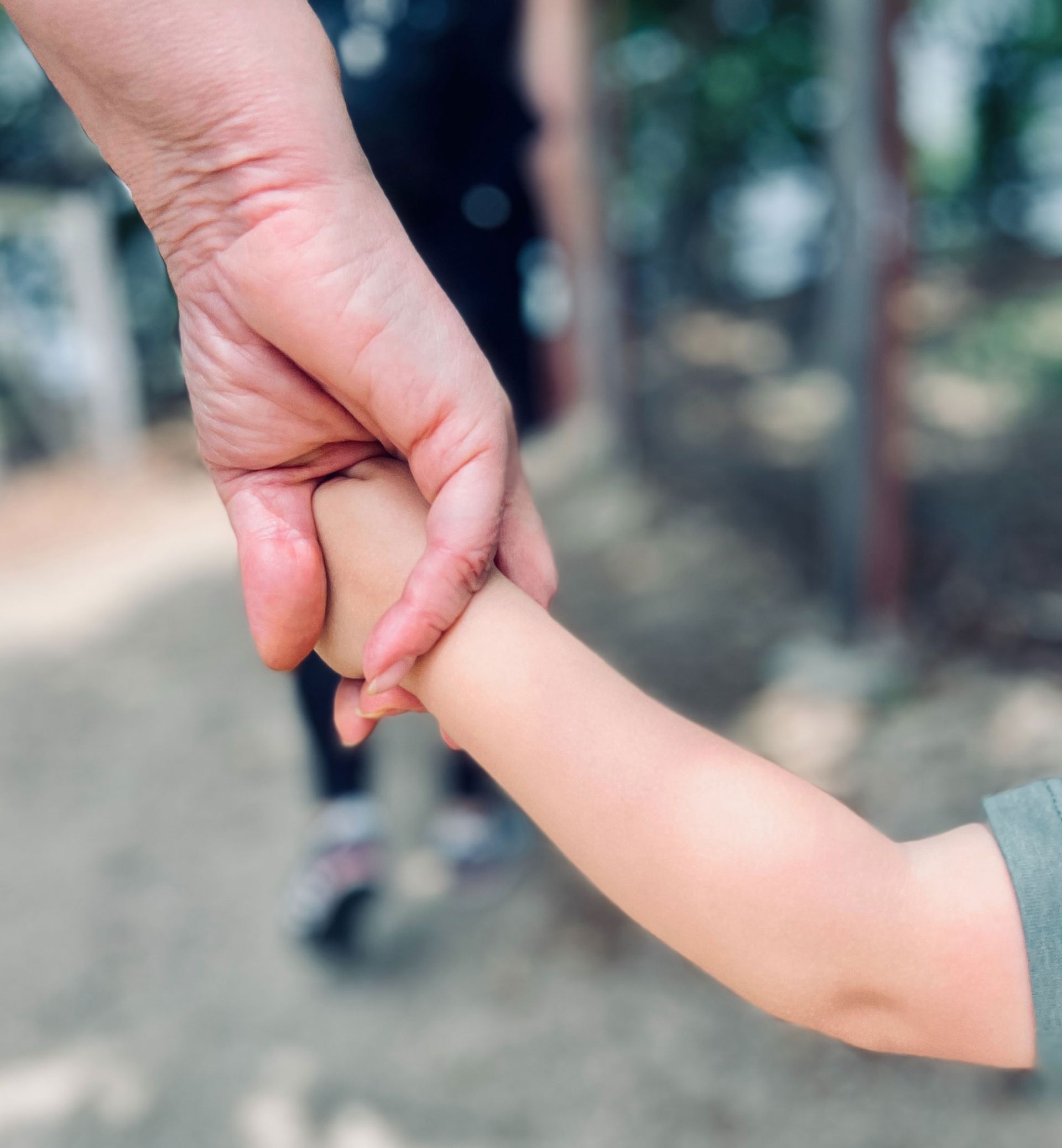 Adult hand holding a small child's hand with a blurry background