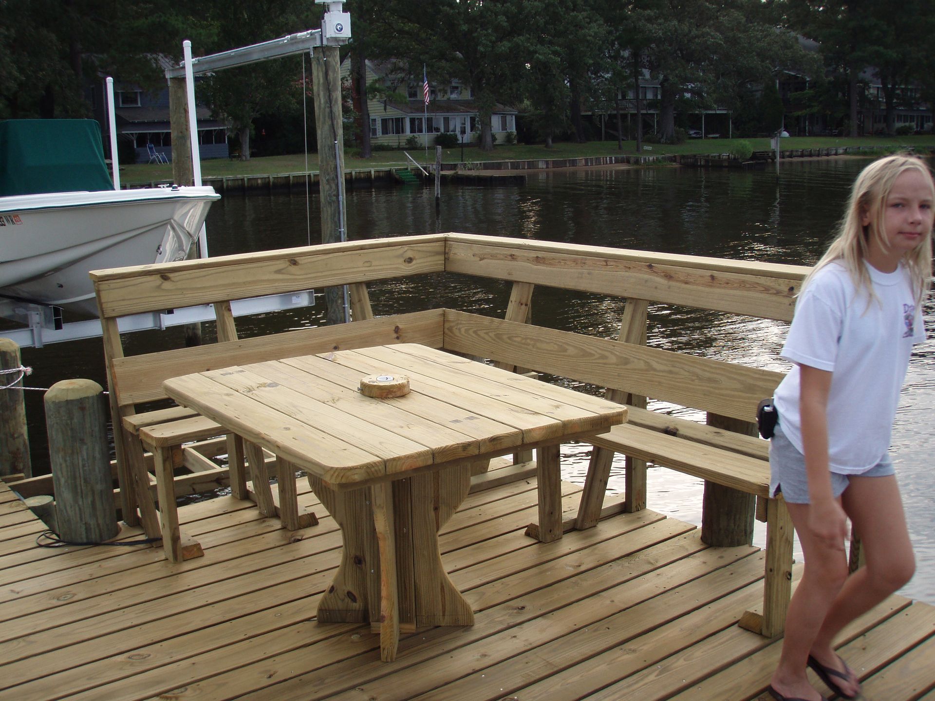 Wooden picnic table and benches on a dock by the water, with a person walking at right.