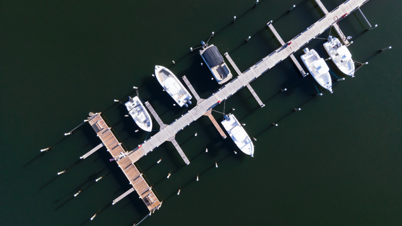 An aerial view of a wooden boat dock extending into dark water, with five white boats moored along its sides.