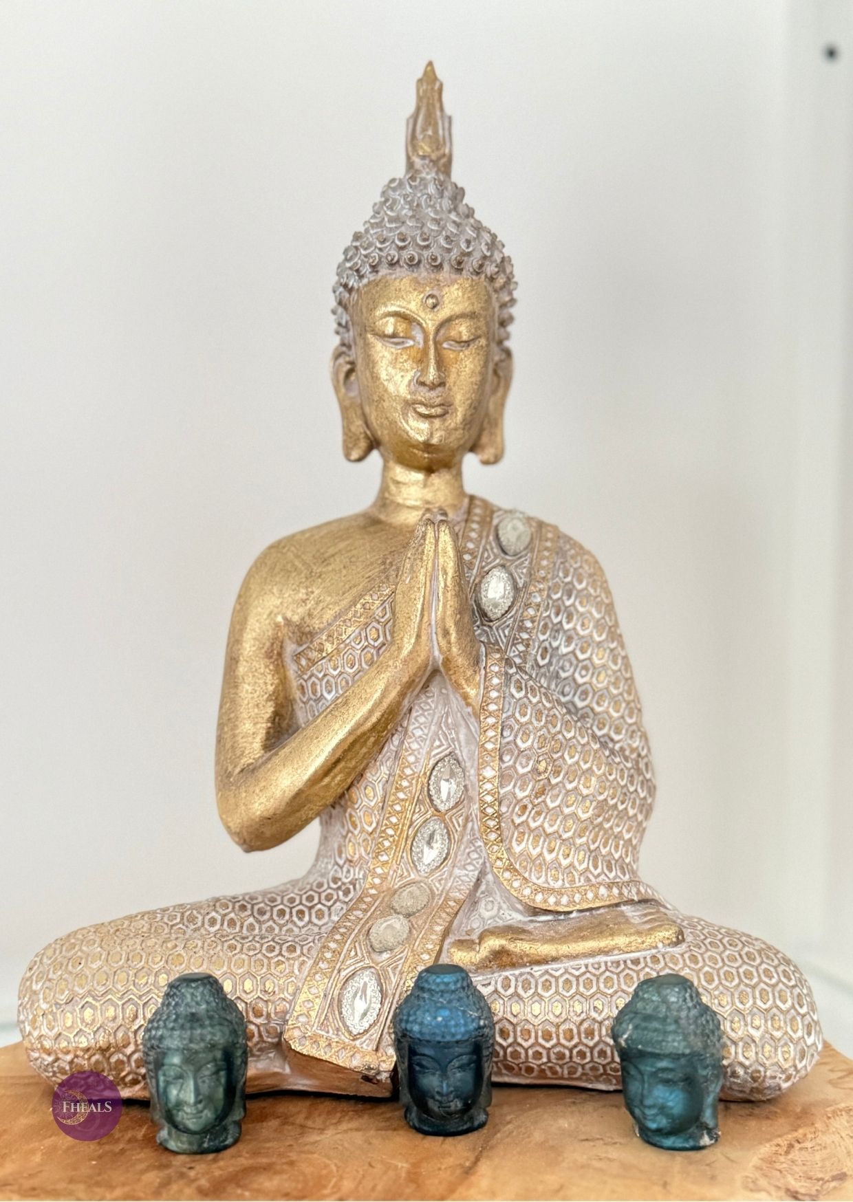 Een goudkleurig Boeddhabeeld in een biddende houding, zittend achter drie kleine, donkergekleurde Boeddha-hoofdjes.