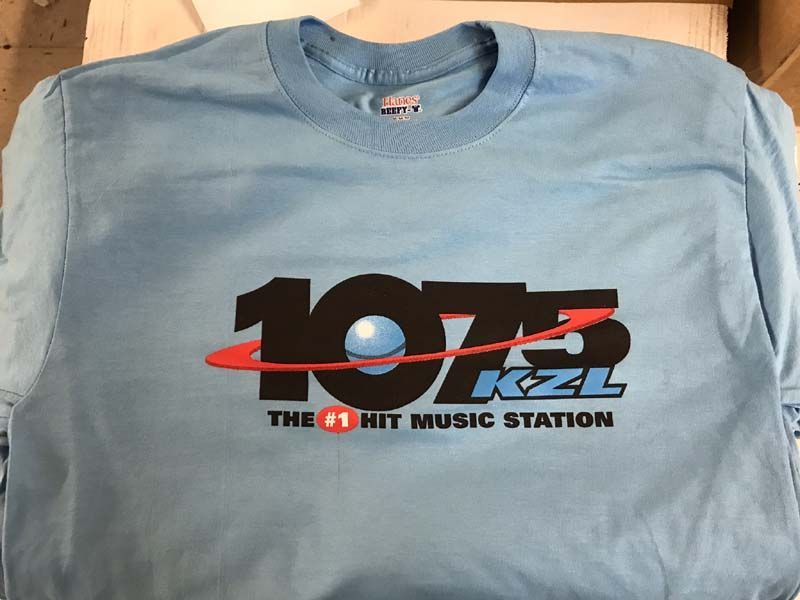 Light blue t-shirt with a black and red logo for radio station 107.5 KZL, 