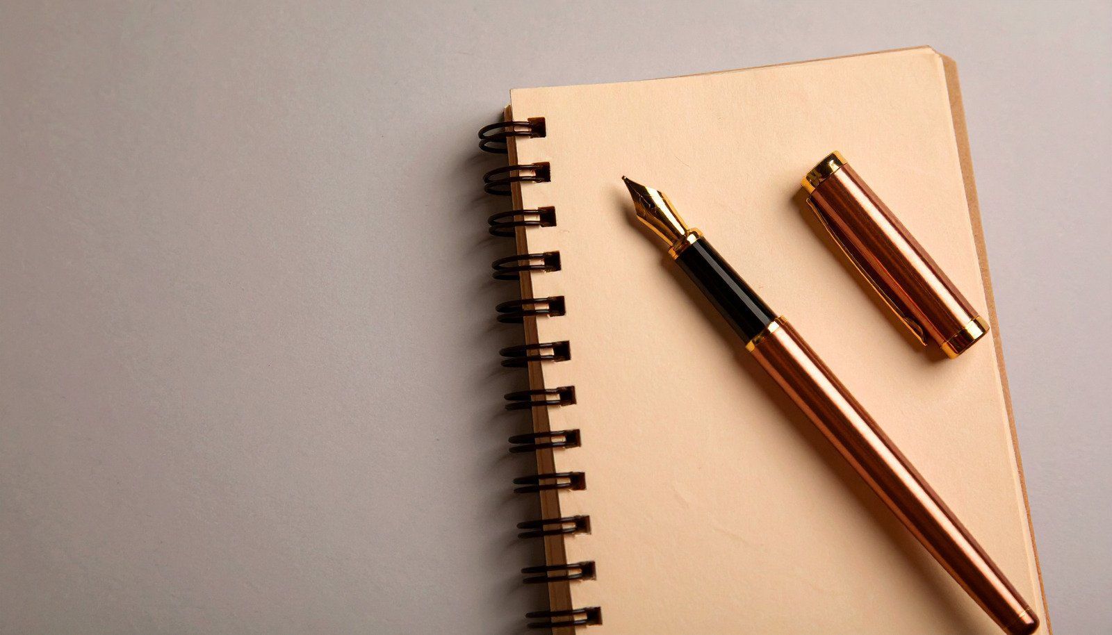 Spiral notebook with gold pen resting on top, pen cap off to the side.