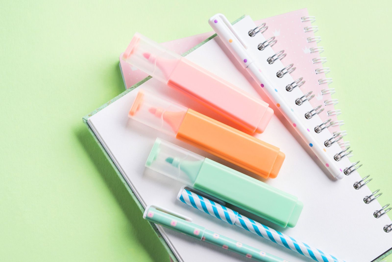 Notebook, highlighters, and pens on a light green surface.