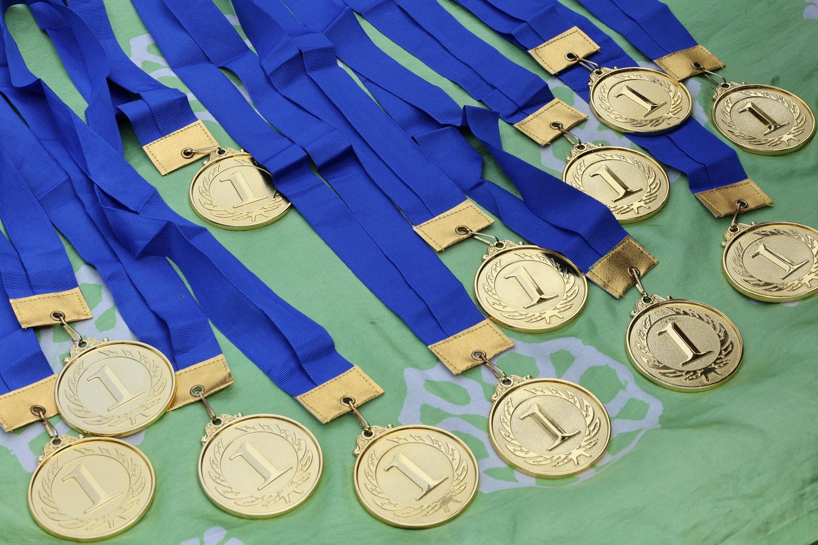 Gold medals with blue ribbons, indicating first place winners, are lying on a green surface.