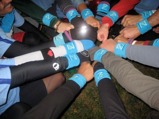 People with blue wristbands huddle together, arms touching a dark sphere.