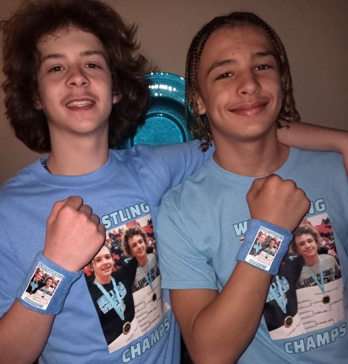 Two young people with light blue shirts and wristbands, posing with fists up.