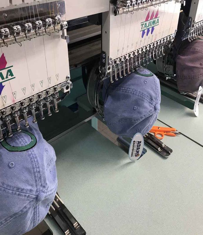 Embroidery machine stitching designs onto blue baseball caps.