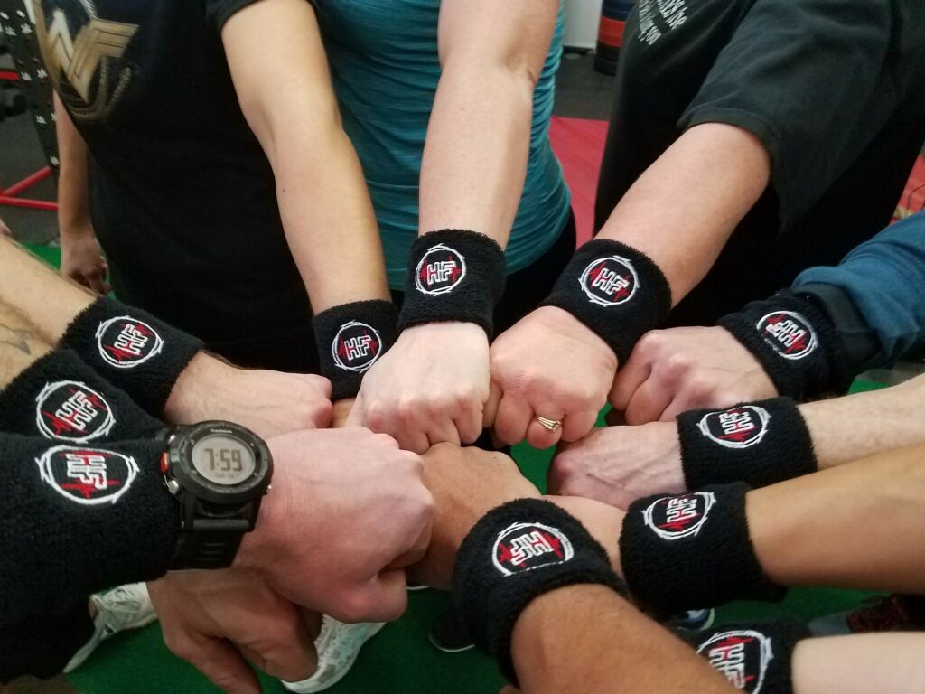Hands with matching black wristbands fist-bumping. The wristbands have a white logo with red accents.