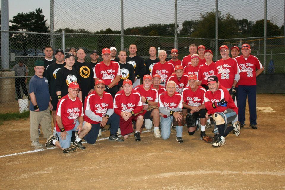 Softball team in red shirts and caps pose on a field. Team name 