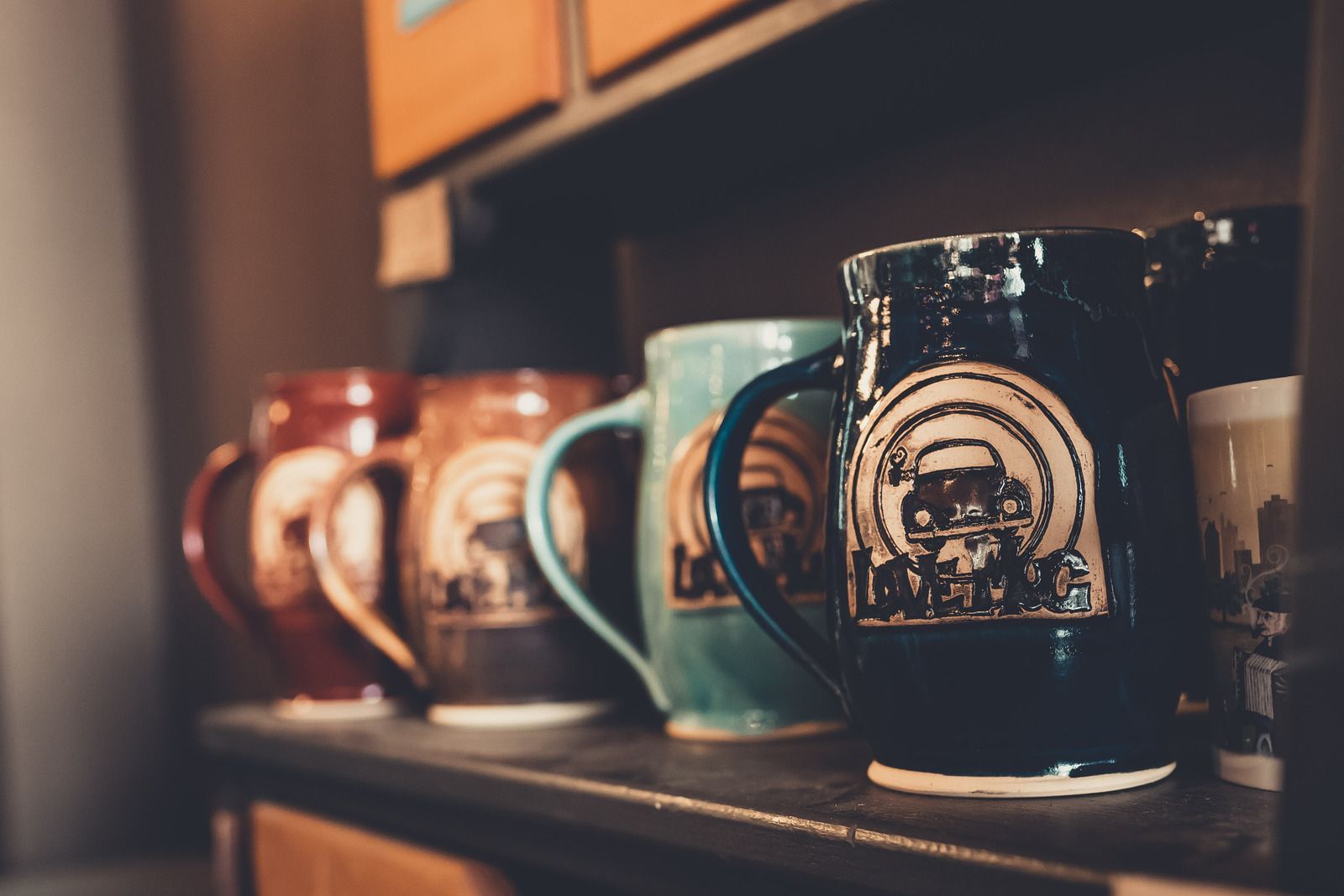 Row of colorful coffee mugs with logos on a shelf.