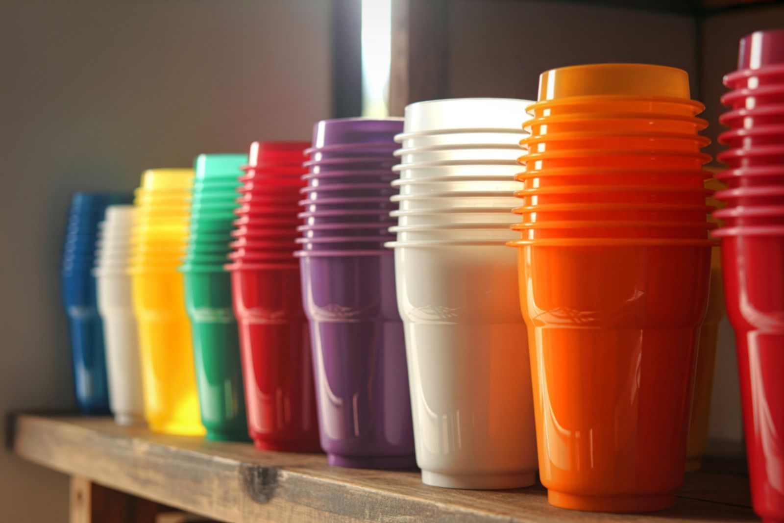 Stacks of colorful plastic cups on a wooden shelf: blue, white, yellow, green, red, purple, white, and orange.