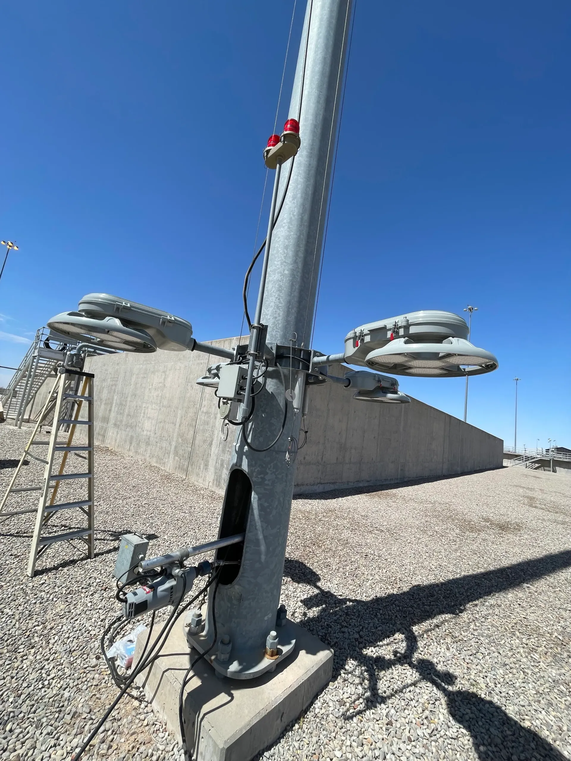 Steel light pole with attached lights, concrete barrier and blue sky.