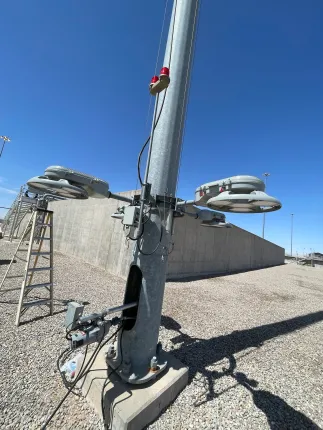 Steel light pole with attached lights, concrete barrier and blue sky.
