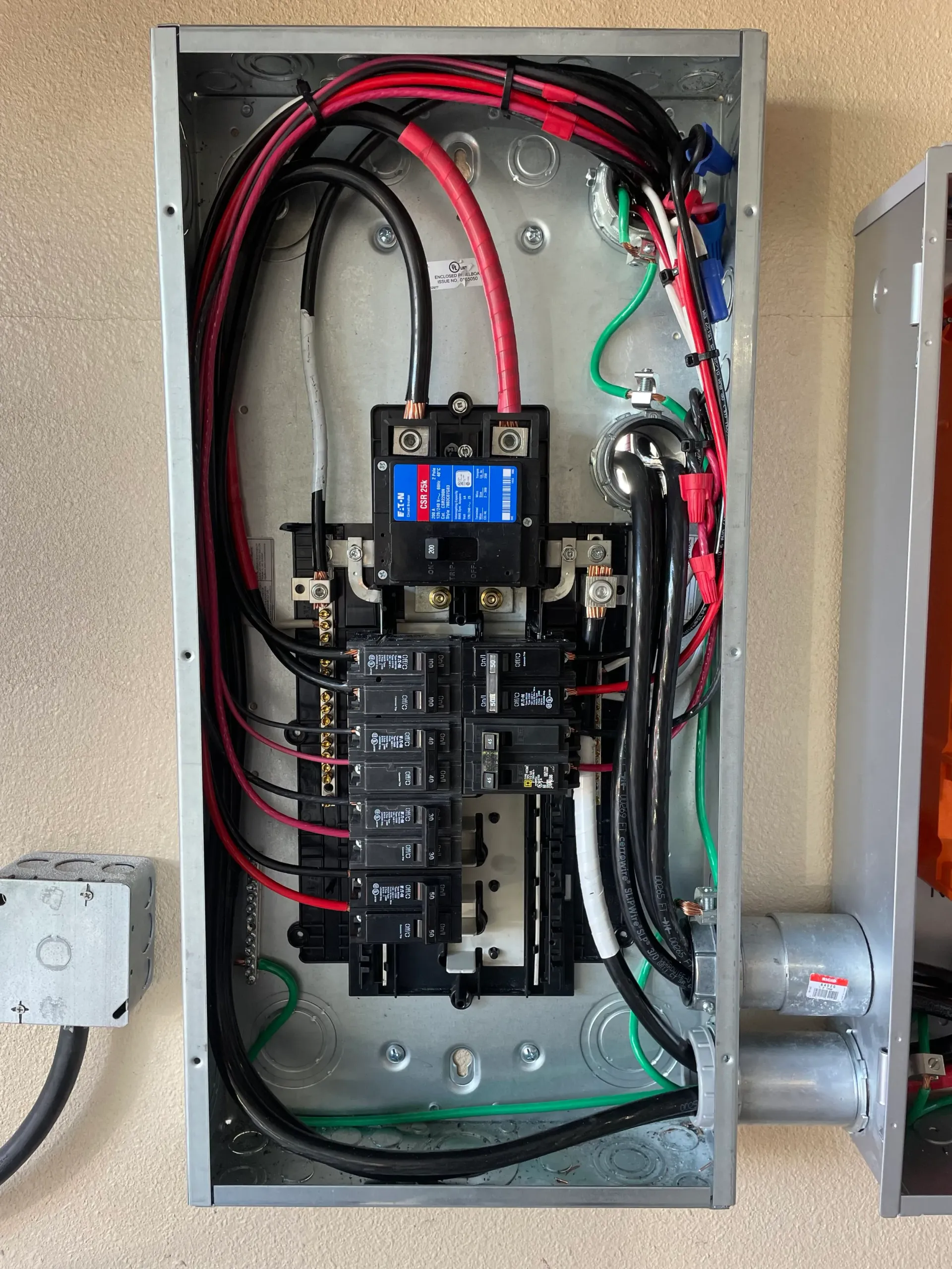 Open electrical panel with black and red wires, circuit breakers, and a digital display.