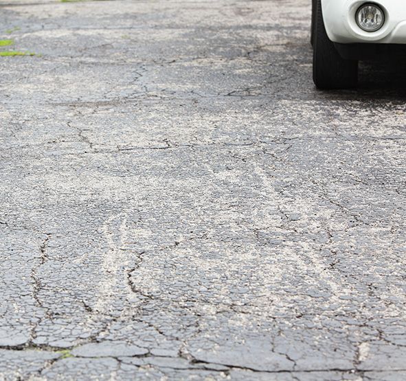 a white car is parked on a cracked asphalt road .