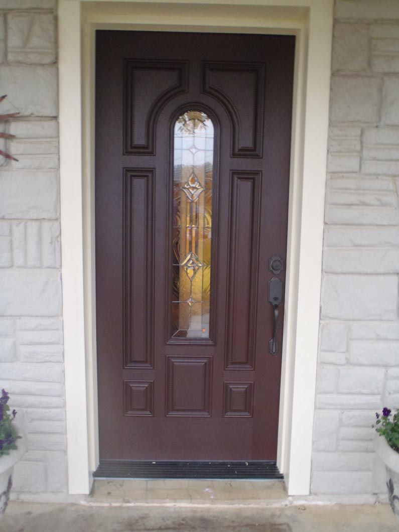 A brown door with a stained glass window is on a brick wall.